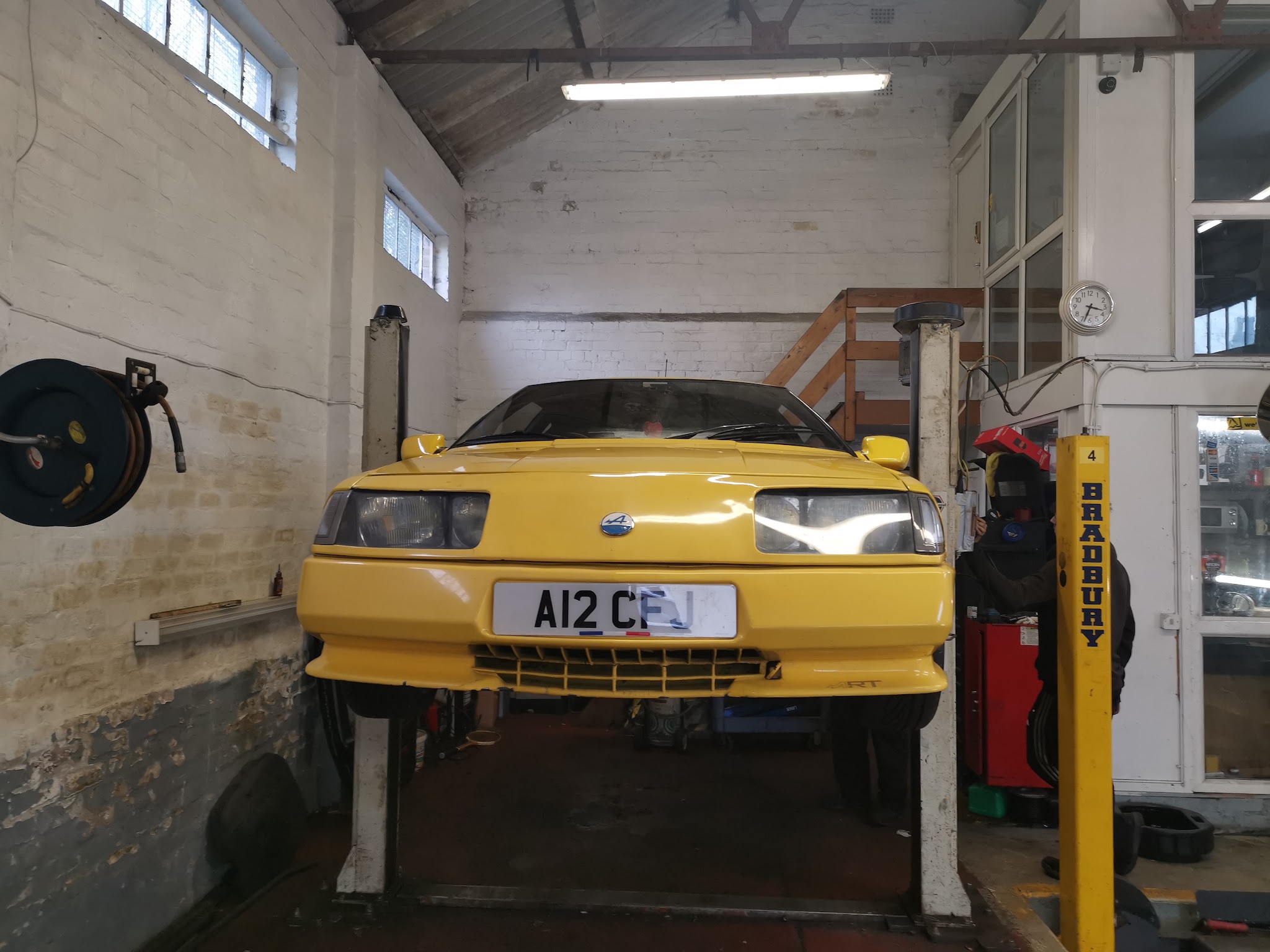 A yellow sports car raised on a two-post lift inside the Lunts Motors workshop